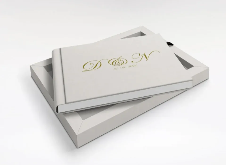 A wedding album in a solid cream cover with a gold monogram, resting on its presentation box