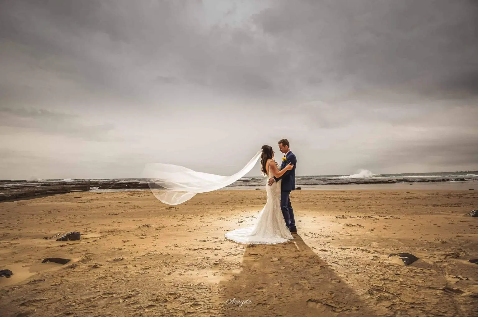 Wedding portrait on a windswept beach beneath a cloudy sky