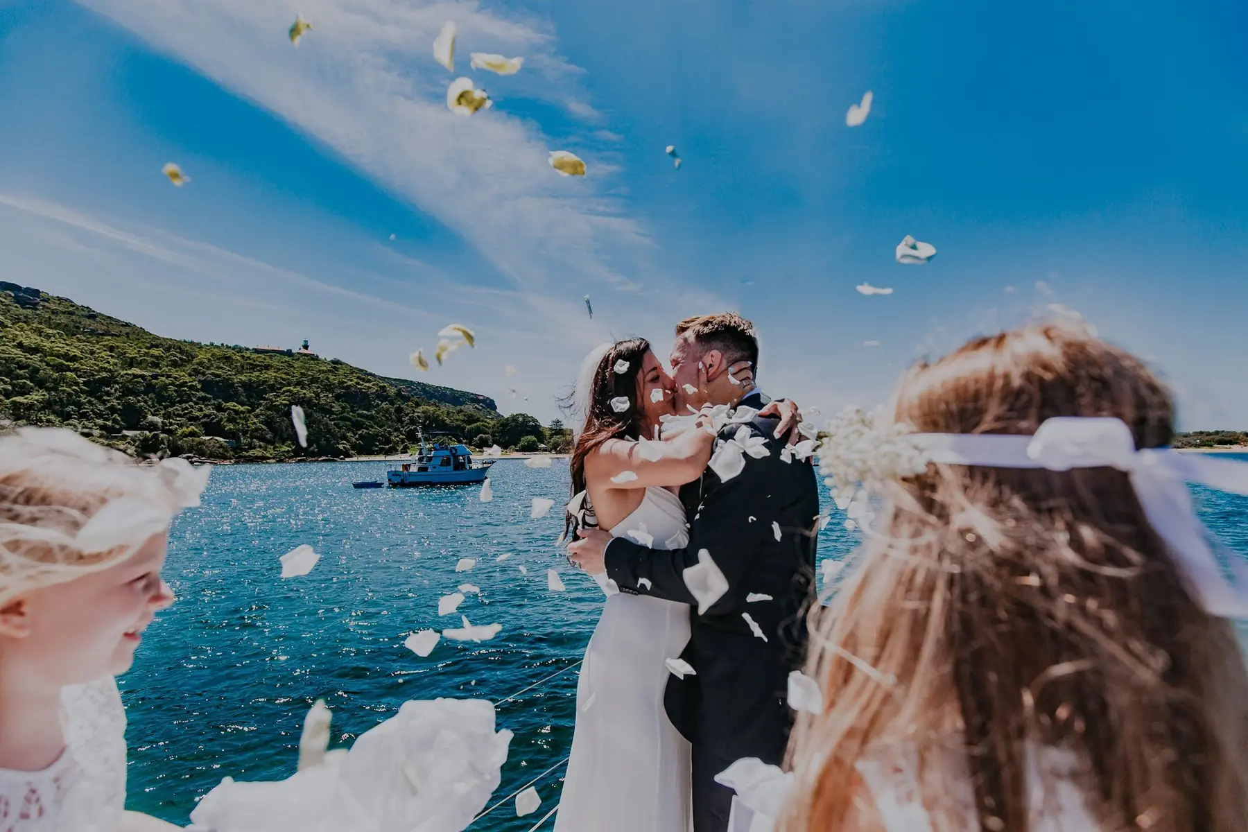 Newlyweds kissing on a boat while guests toss petals around them