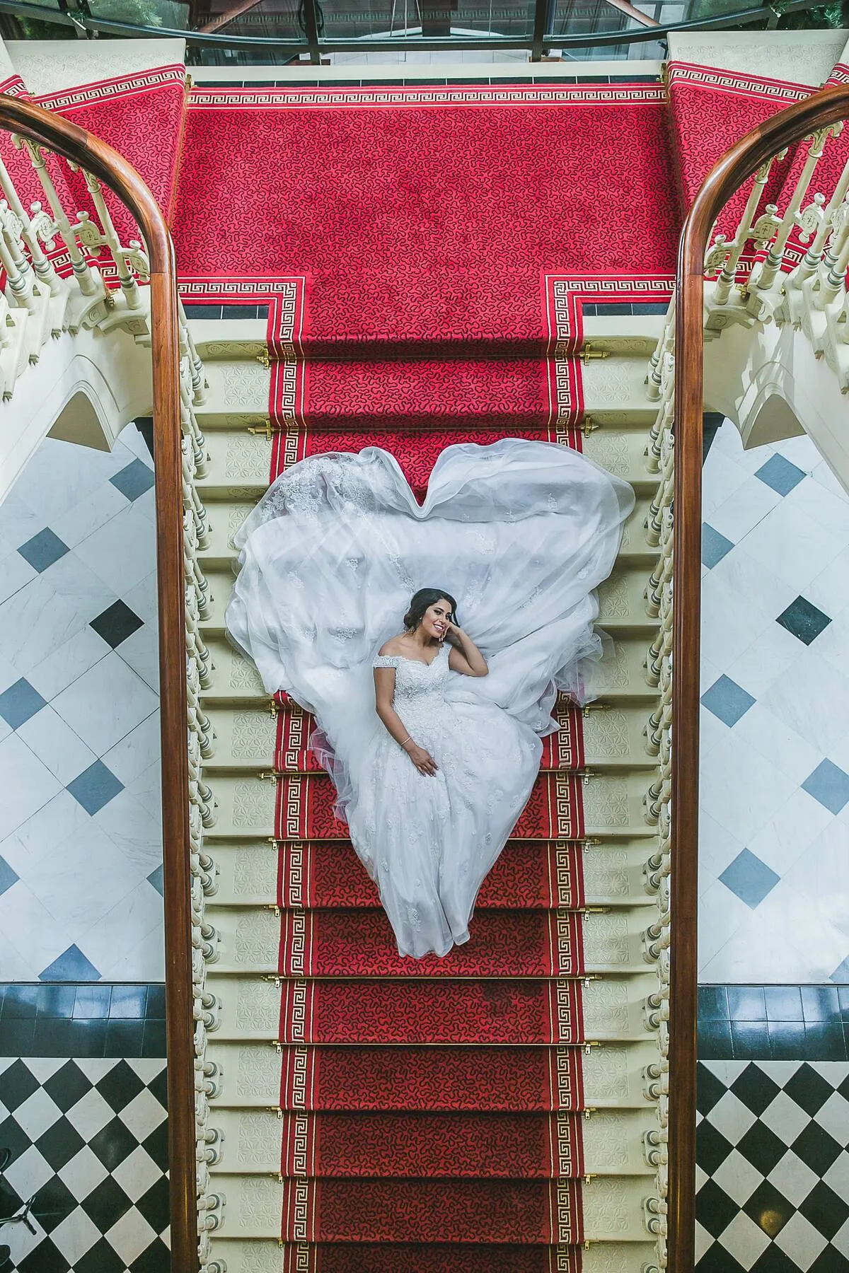 Yostina lying on a red-carpeted staircase in a white wedding dress