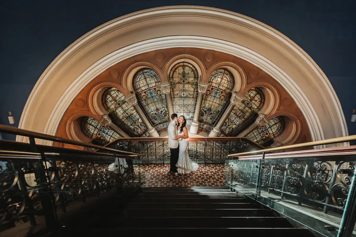 A couple standing together on the QVB staircase beneath a stained-glass dome in Sydney CBD