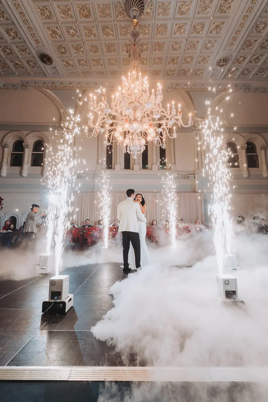 A couple dancing in The Tea Room, QVB beneath a chandelier with red florals, fog and indoor sparklers