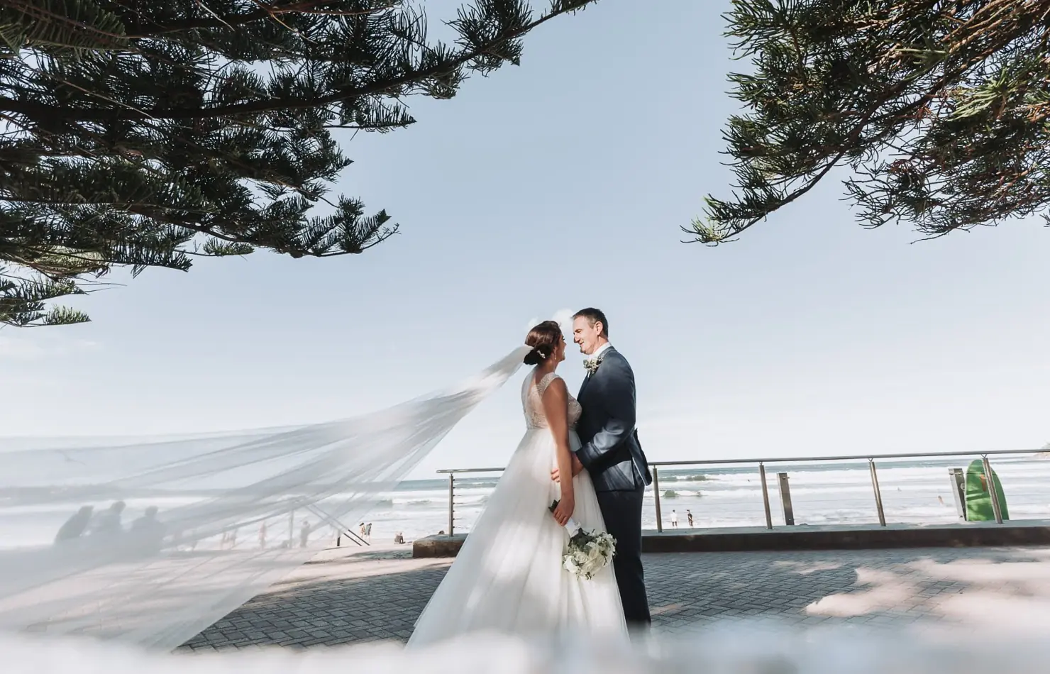 A couple standing by the ocean at Manly Golf Club in Sydney’s Northern Beaches with the veil carried across the frame