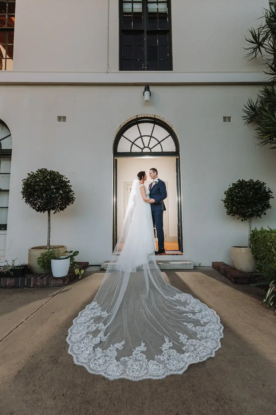 A couple standing together in an arched doorway at Manly Golf Club in Sydney’s Northern Beaches with the veil trailing across the path