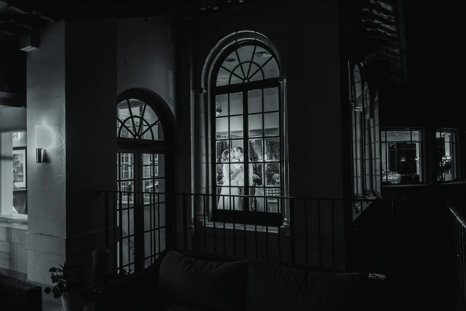 Megan and Scott embracing through arched windows at Manly Golf Club