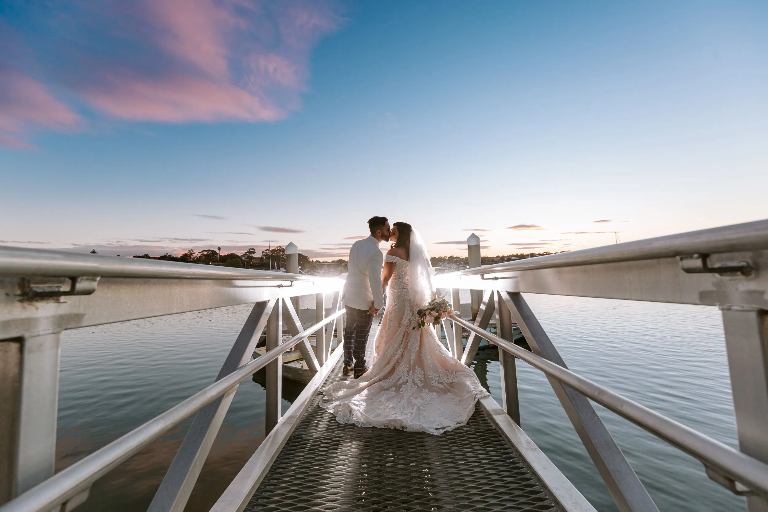 A newlywed couple kissing on a sunset marina walkway