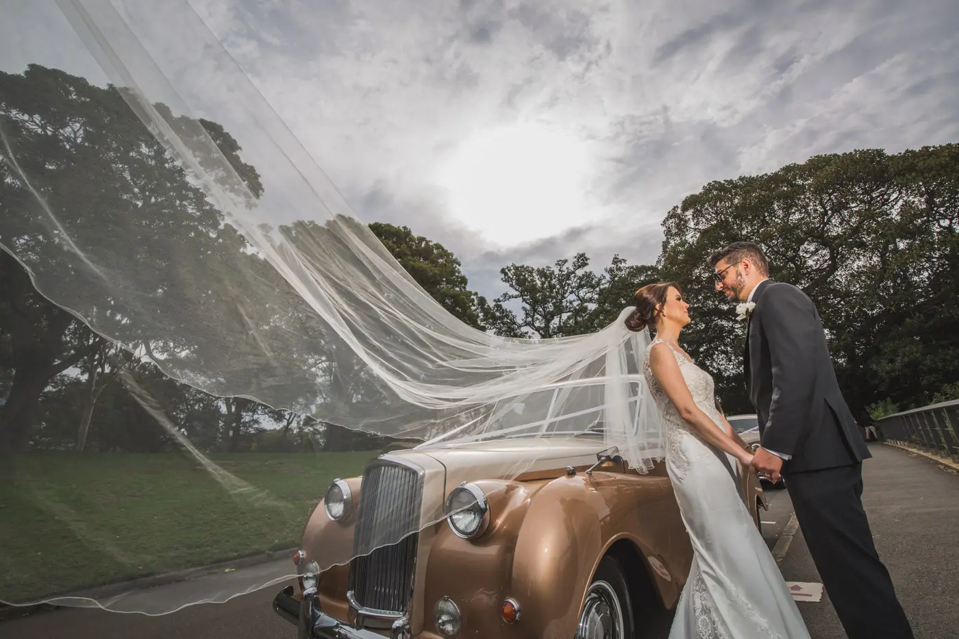 Wedding portrait beside a vintage car beneath a flowing veil
