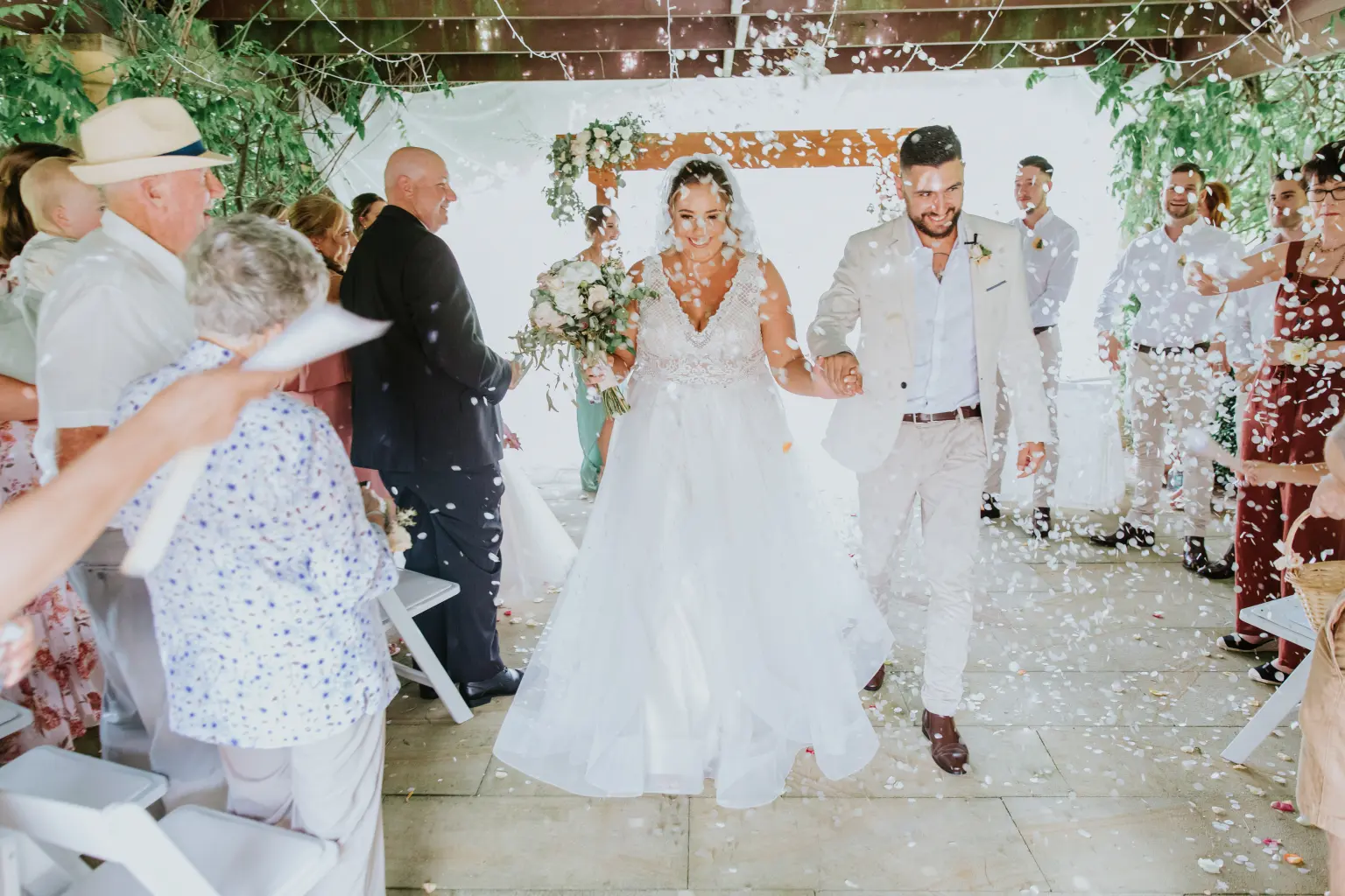 Wedding celebration beneath a floral arch with confetti in the air