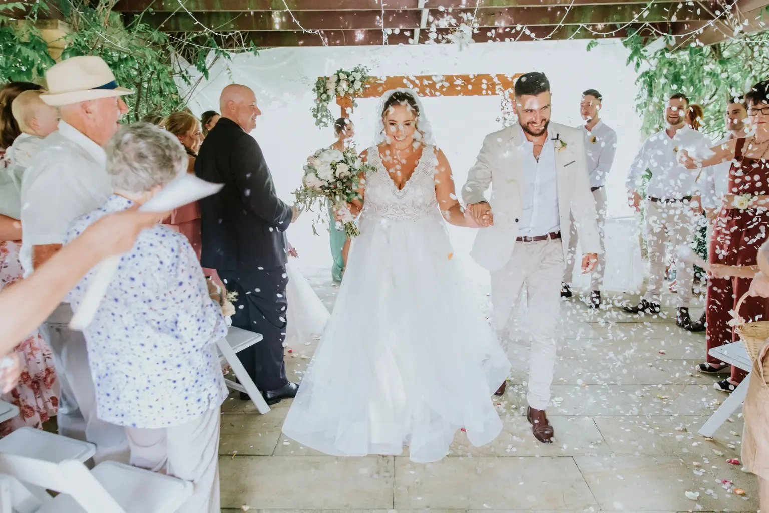 Wedding celebration beneath a floral arch with confetti in the air