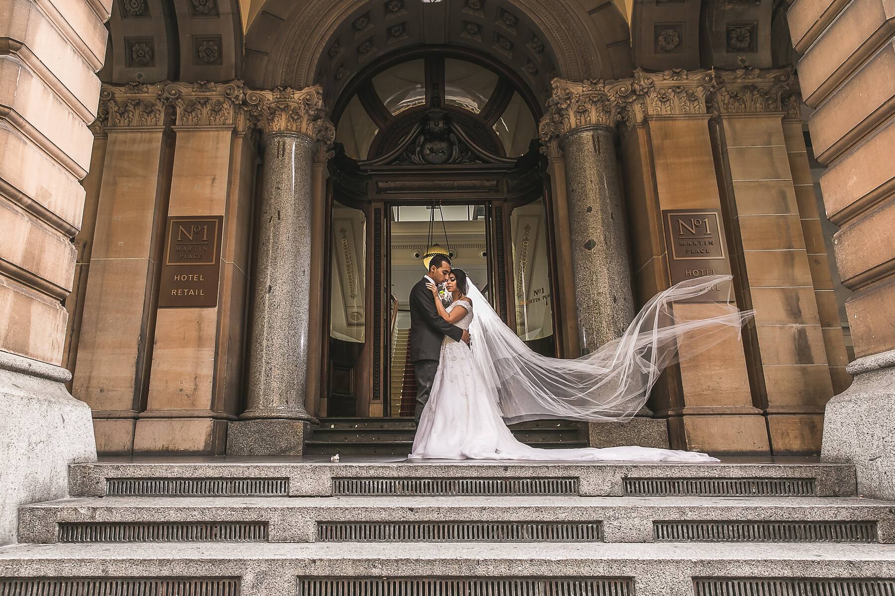 Fady and Yostina standing together at the entrance to No. 1 Martin Place, with Yostina’s veil extending across the steps