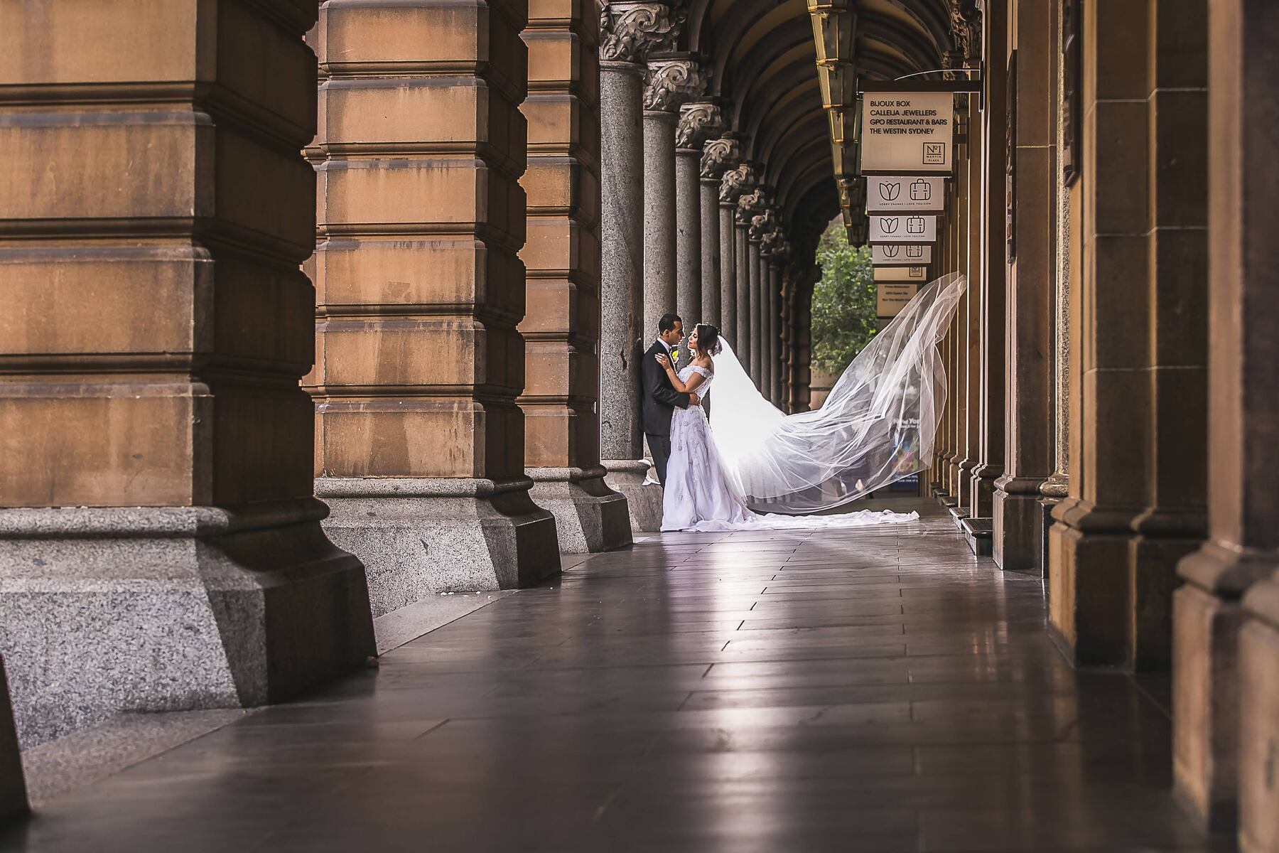 Fady and Yostina standing together beneath the stone arcade at Martin Place with the veil flowing behind Yostina