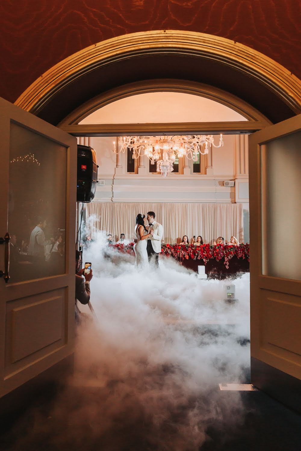 Ivana and Ivan sharing a dance in The Tea Room beneath a chandelier, red florals and low fog