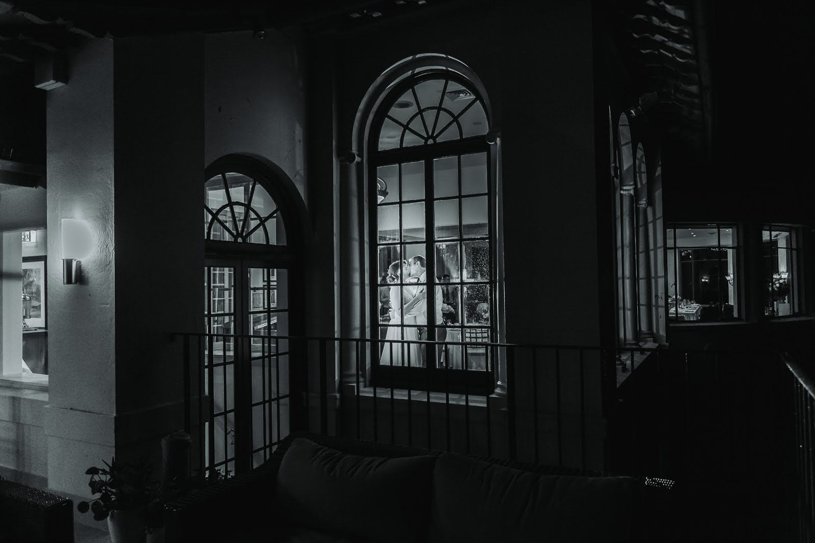Megan and Scott embracing through arched windows at Manly Golf Club